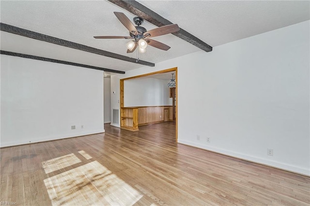 empty room with beam ceiling, visible vents, a ceiling fan, a textured ceiling, and wood finished floors