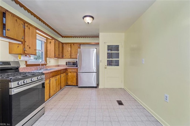 kitchen featuring baseboards, brown cabinetry, appliances with stainless steel finishes, light countertops, and a sink