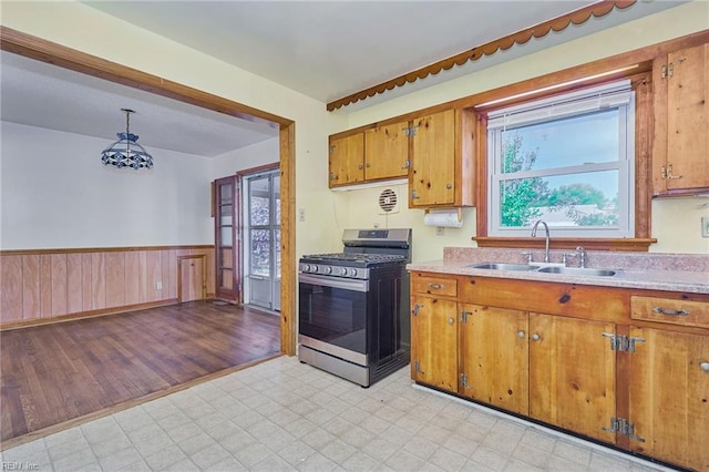 kitchen with stainless steel gas range oven, a sink, light countertops, wainscoting, and brown cabinets