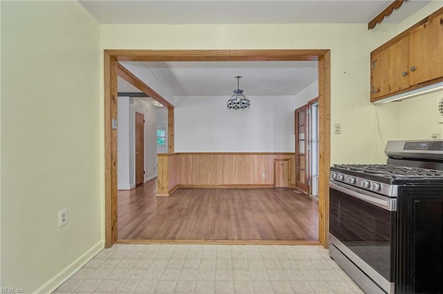 kitchen with stainless steel gas range, a wainscoted wall, decorative light fixtures, and light floors