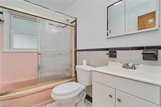 bathroom with tile walls, toilet, wainscoting, enclosed tub / shower combo, and vanity