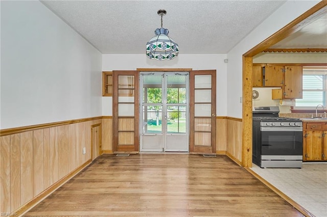 interior space with a wainscoted wall, light wood-style flooring, a textured ceiling, french doors, and a sink