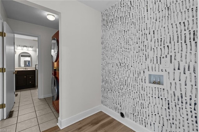 laundry area with stacked washing maching and dryer, a sink, light tile patterned flooring, and baseboards