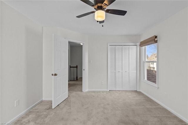 unfurnished bedroom featuring baseboards, ceiling fan, a closet, and light colored carpet