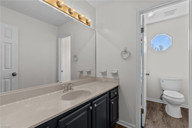 bathroom with toilet, wood finished floors, visible vents, vanity, and baseboards