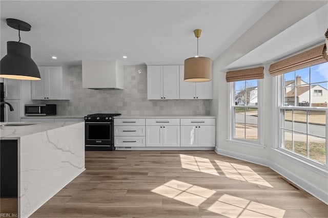 kitchen featuring range with gas stovetop, stainless steel microwave, light wood-style flooring, decorative backsplash, and white cabinets