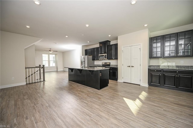 kitchen featuring light wood-style flooring, a breakfast bar, open floor plan, stainless steel appliances, and dark cabinetry