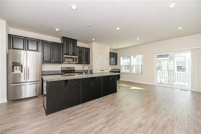 kitchen with a breakfast bar, a sink, light wood-style floors, appliances with stainless steel finishes, and a center island with sink