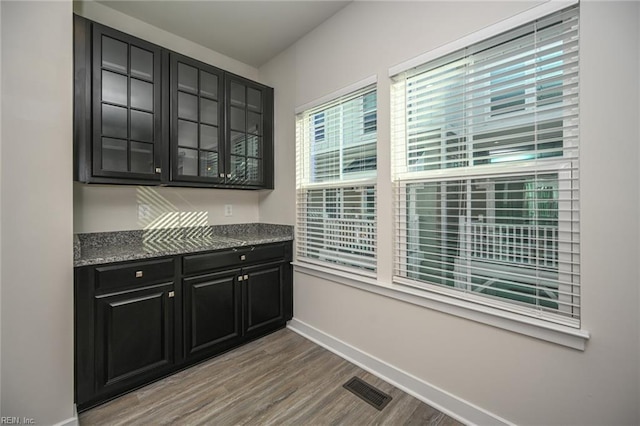 kitchen with visible vents, glass insert cabinets, wood finished floors, dark cabinets, and baseboards