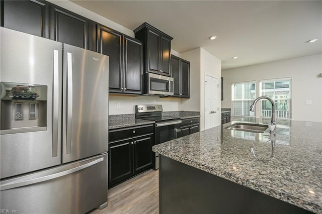 kitchen with dark cabinets, dark stone countertops, stainless steel appliances, and a sink