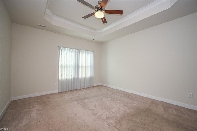 carpeted empty room with a raised ceiling, visible vents, ornamental molding, a ceiling fan, and baseboards