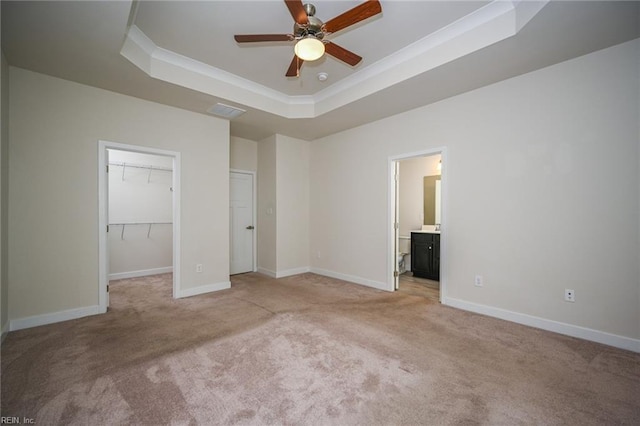 unfurnished bedroom featuring a raised ceiling, light colored carpet, a spacious closet, ornamental molding, and baseboards