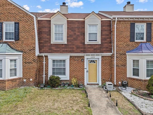 view of front facade with a front yard, roof with shingles, a chimney, and brick siding