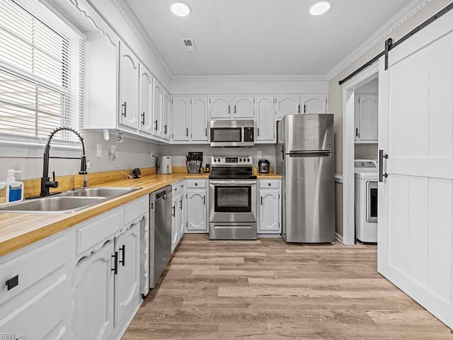 kitchen with a barn door, stainless steel appliances, a sink, white cabinets, and washer / clothes dryer