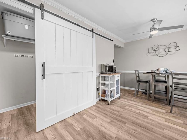 unfurnished dining area featuring a barn door, wood finished floors, a ceiling fan, baseboards, and crown molding