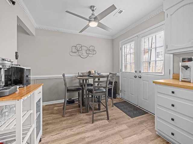 dining space with ceiling fan, light wood finished floors, visible vents, and crown molding