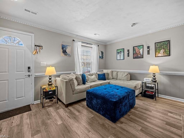 living room featuring a wainscoted wall, ornamental molding, wood finished floors, and visible vents