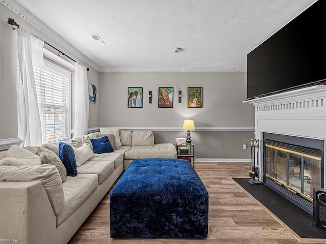 living area with a fireplace with flush hearth, wood finished floors, baseboards, visible vents, and crown molding