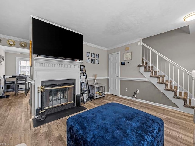 living area featuring a fireplace with flush hearth, wood finished floors, stairs, ornamental molding, and wainscoting