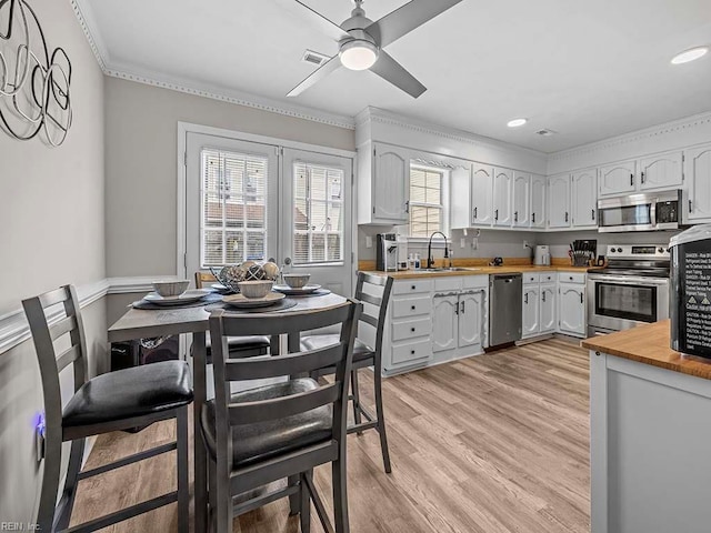 kitchen featuring white cabinets, light wood-style flooring, appliances with stainless steel finishes, wooden counters, and a sink