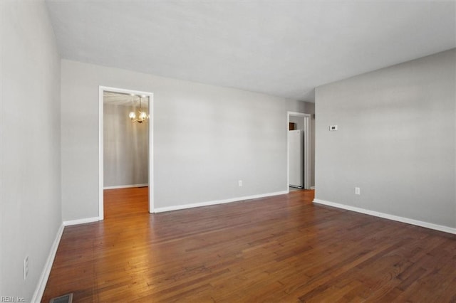 empty room with a chandelier, wood finished floors, and baseboards