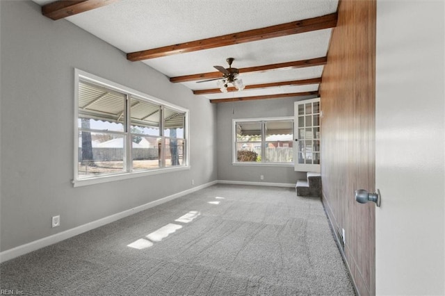 carpeted empty room with beam ceiling, ceiling fan, a textured ceiling, and baseboards