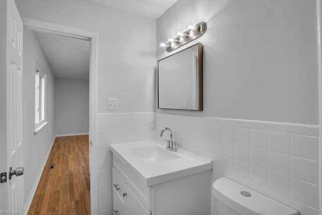 half bath with tile walls, toilet, wainscoting, vanity, and wood finished floors