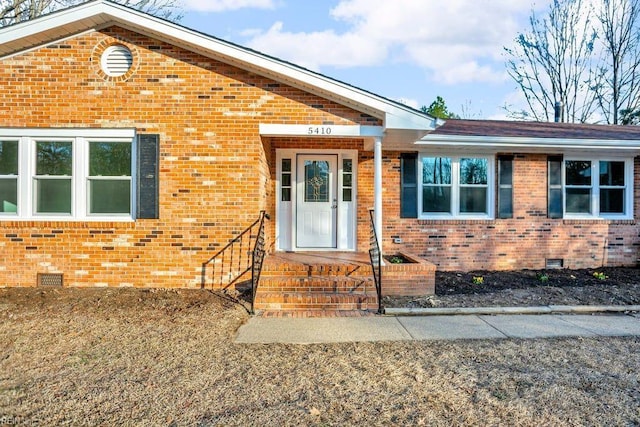 view of exterior entry with brick siding and crawl space