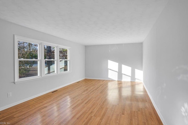 empty room featuring baseboards, a textured ceiling, and light wood finished floors