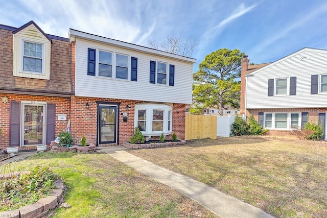 multi unit property featuring roof with shingles, fence, a front lawn, and brick siding