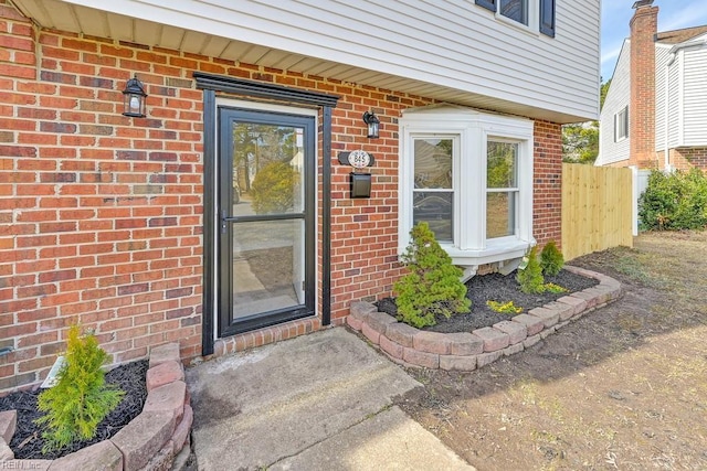 view of exterior entry featuring brick siding and fence