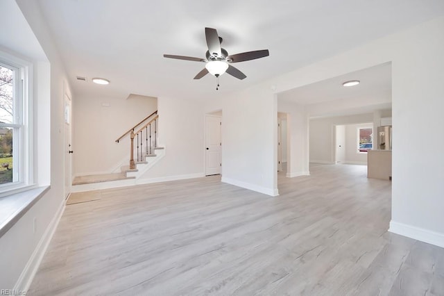 unfurnished living room featuring stairs, light wood finished floors, a wealth of natural light, and baseboards