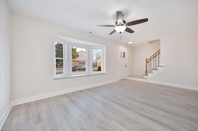 interior space featuring baseboards, visible vents, a ceiling fan, stairway, and light wood-style floors