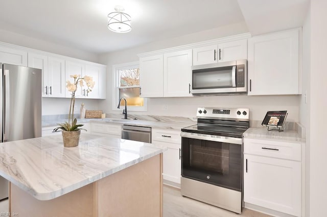 kitchen featuring light stone countertops, stainless steel appliances, a sink, white cabinets, and a center island