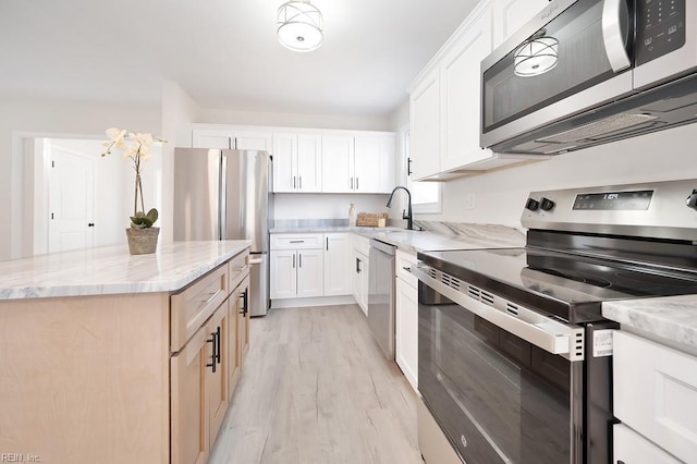 kitchen featuring light stone counters, a center island, stainless steel appliances, light wood-style floors, and a sink