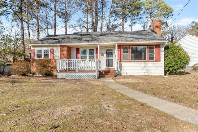 view of front of house with covered porch, a chimney, brick siding, and a front yard