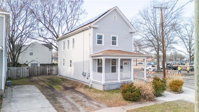 view of front of property featuring a porch, roof mounted solar panels, and fence