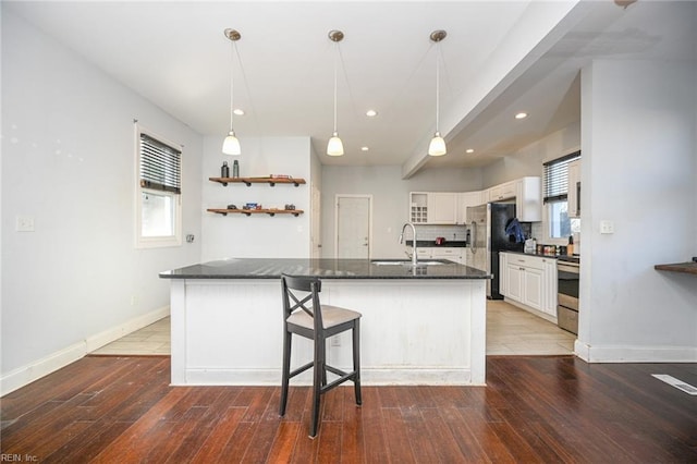 kitchen with stainless steel appliances, a sink, white cabinetry, baseboards, and hardwood / wood-style floors