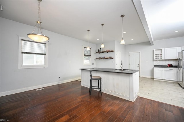 kitchen featuring a sink, light wood-type flooring, open shelves, dark countertops, and stainless steel fridge