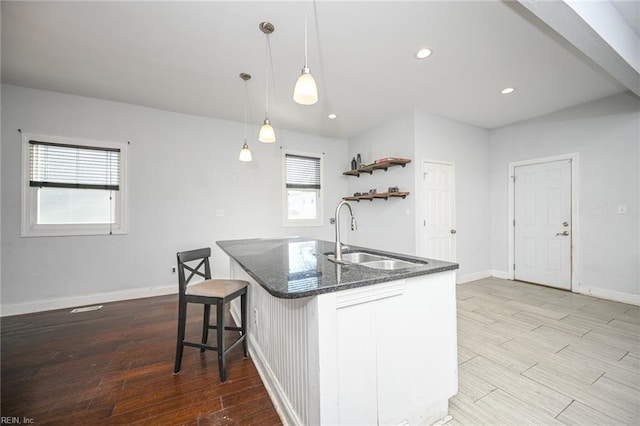 kitchen featuring wood finished floors, a sink, baseboards, hanging light fixtures, and dark stone countertops