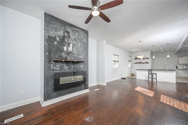 unfurnished living room featuring a large fireplace, dark wood-type flooring, a sink, and baseboards