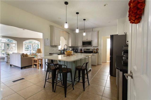 kitchen with visible vents, backsplash, freestanding refrigerator, stainless steel microwave, and a kitchen bar