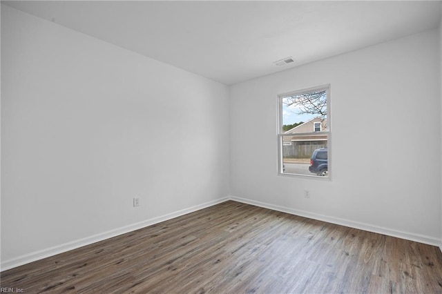 empty room with wood finished floors, visible vents, and baseboards