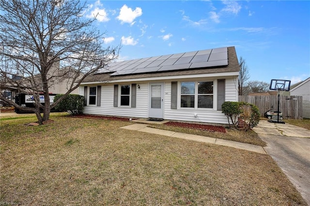 view of front facade with roof with shingles, a front yard, fence, and roof mounted solar panels