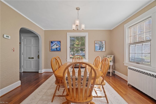 dining area featuring baseboards, arched walkways, radiator heating unit, wood finished floors, and a notable chandelier