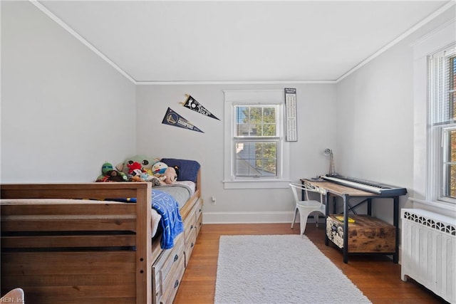 bedroom with radiator heating unit, crown molding, baseboards, and wood finished floors