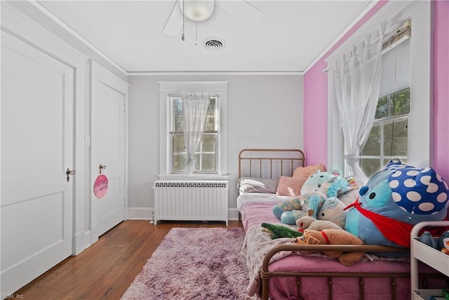 bedroom featuring ornamental molding, radiator, visible vents, and wood finished floors