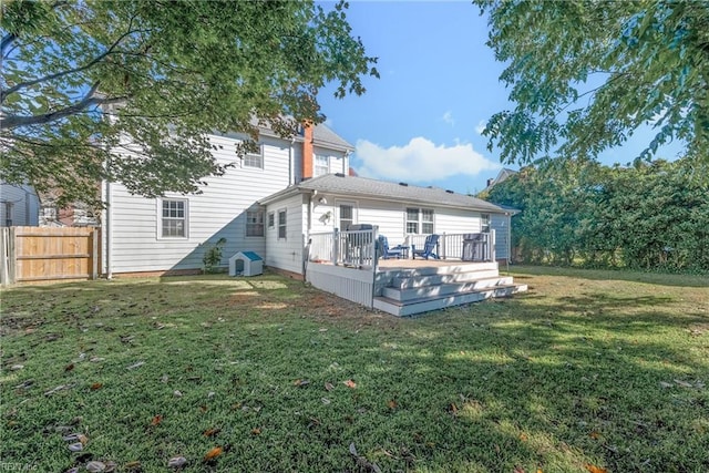 rear view of house featuring fence, a deck, and a lawn