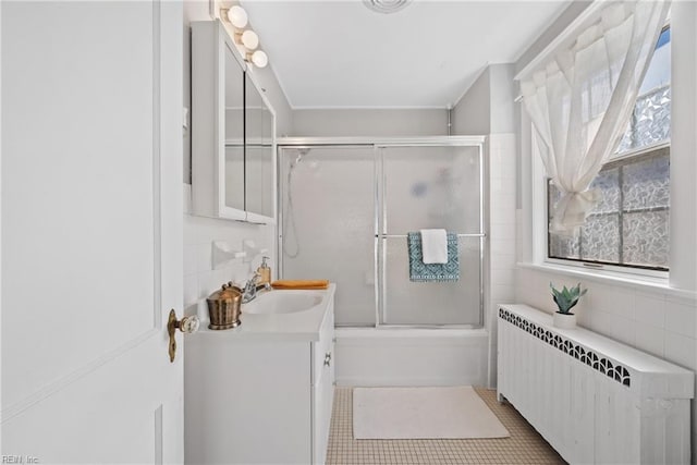 full bathroom with combined bath / shower with glass door, radiator heating unit, vanity, and tile walls