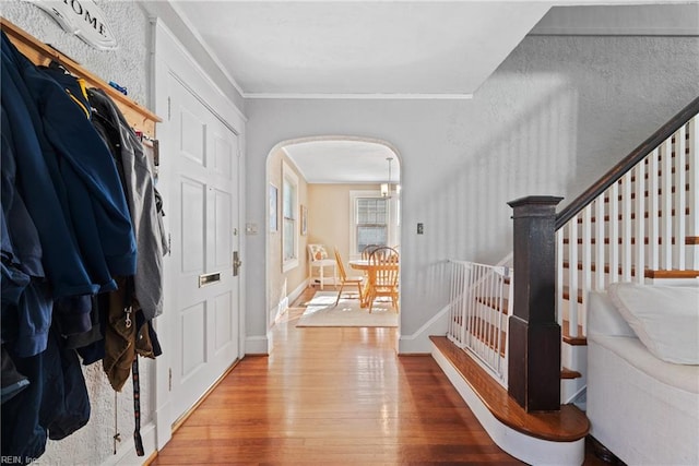 entrance foyer with arched walkways, crown molding, stairway, wood finished floors, and baseboards